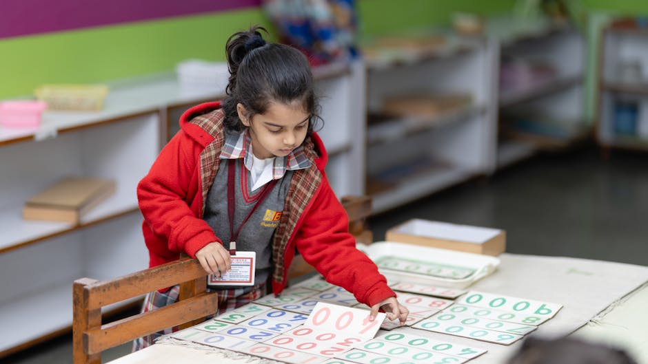 A young child in a red jacket learns numbers using educational tools in a classroom setting
